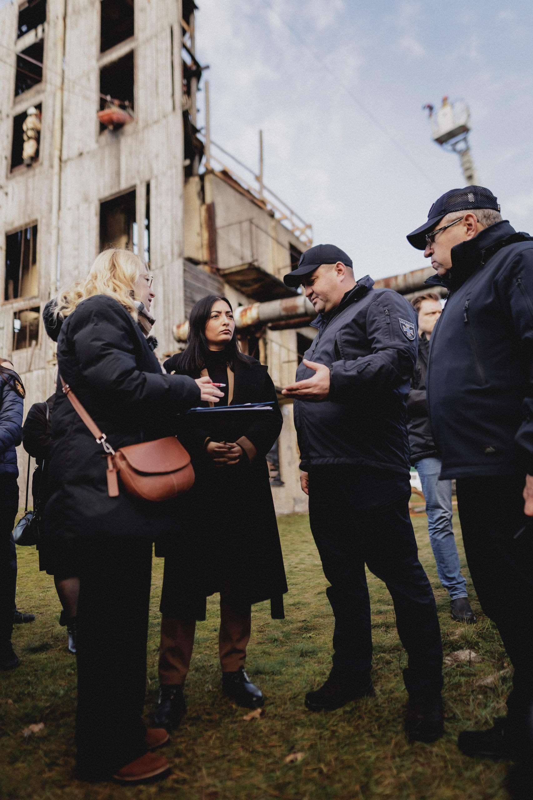 Reem Alabali Radovan mit Vertretern des ukrainischen Katastrophenschutzes vor einem zerstörten Gebäude