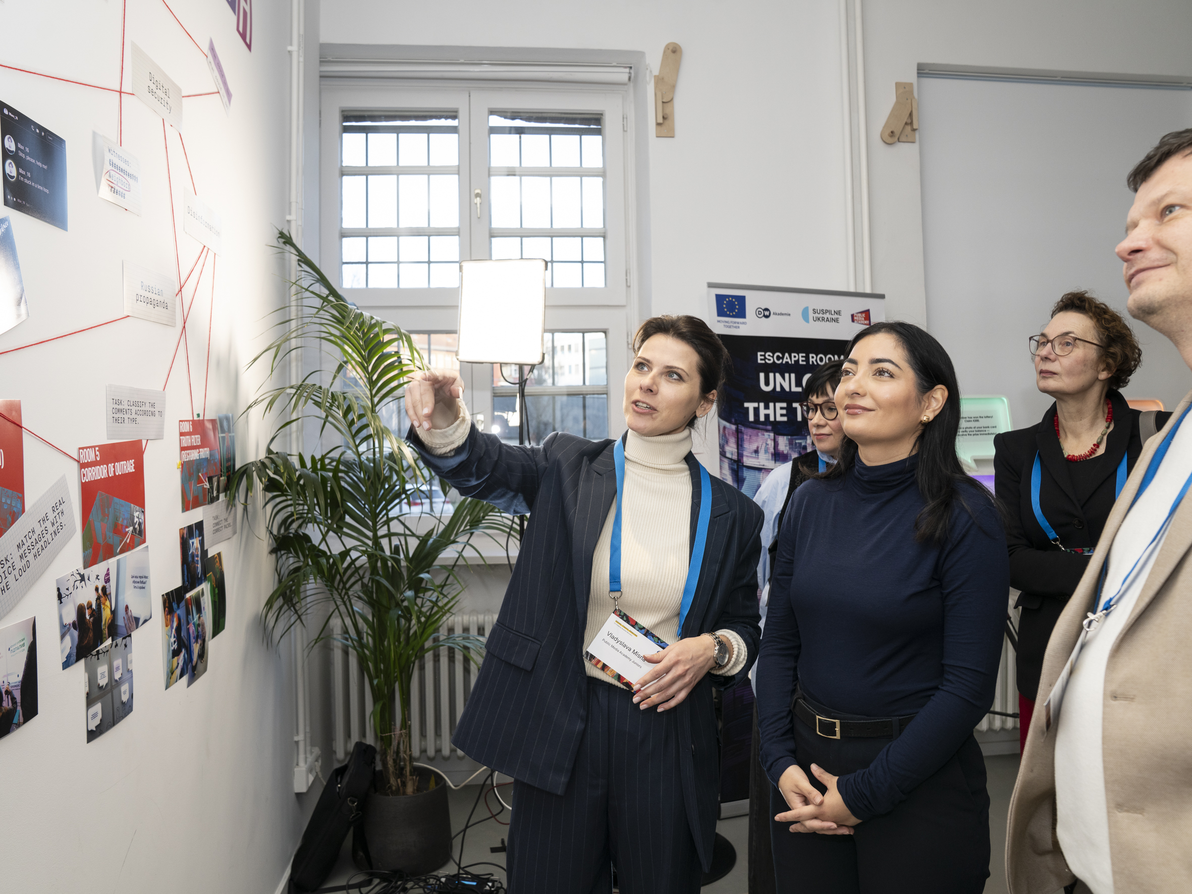 Foto von mehreren Frauen, eine davon zeigt auf eine Wand mit Bildern.