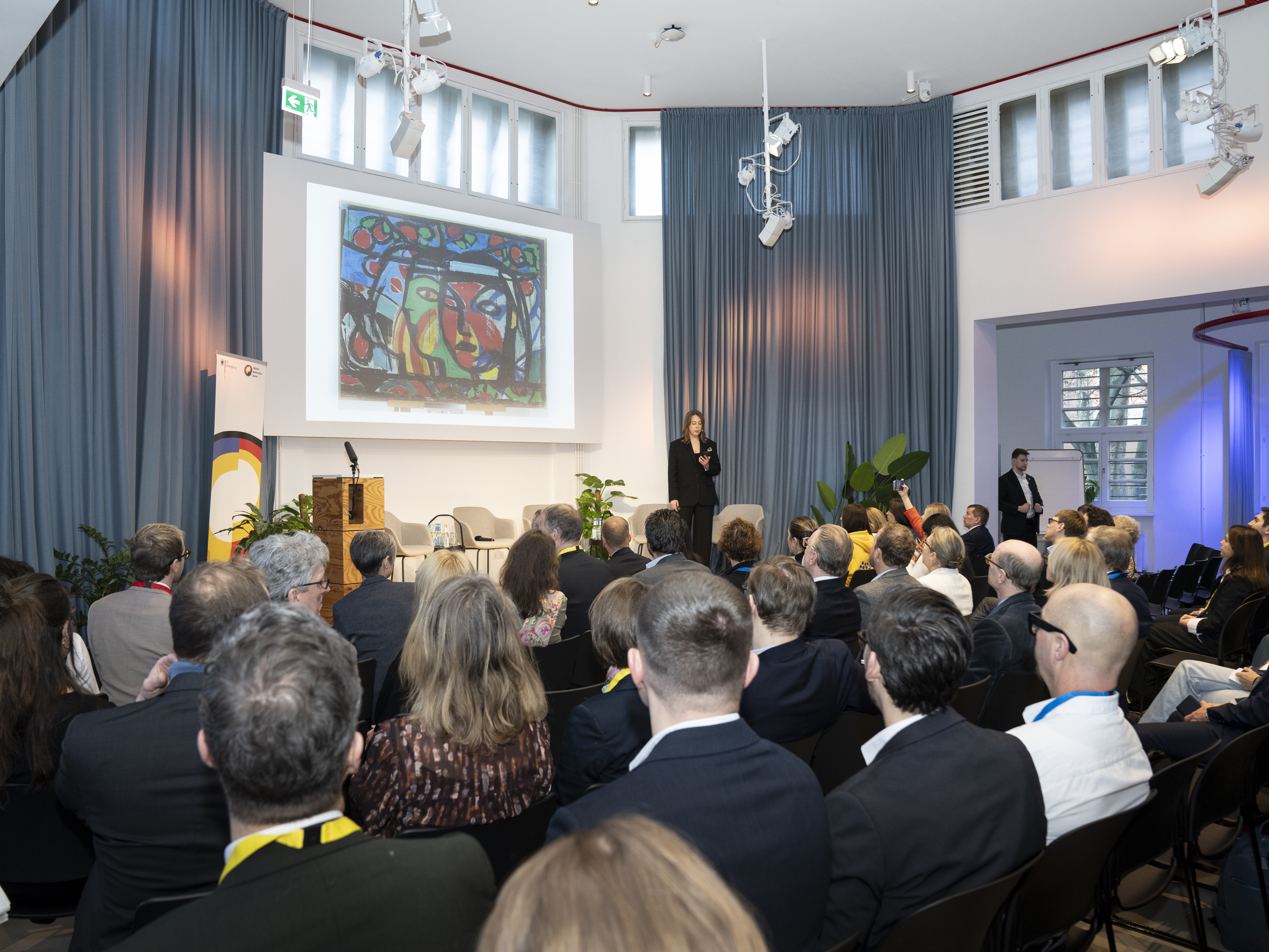 Foto von einer Frau auf einer Bühne, die vor vielen Menschen spricht.