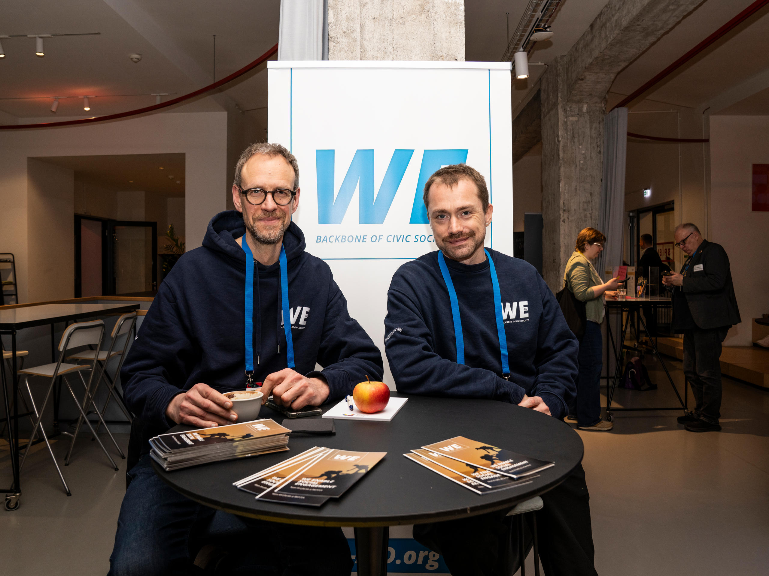Zwei Männer vor einem weiß-blauen Plakat