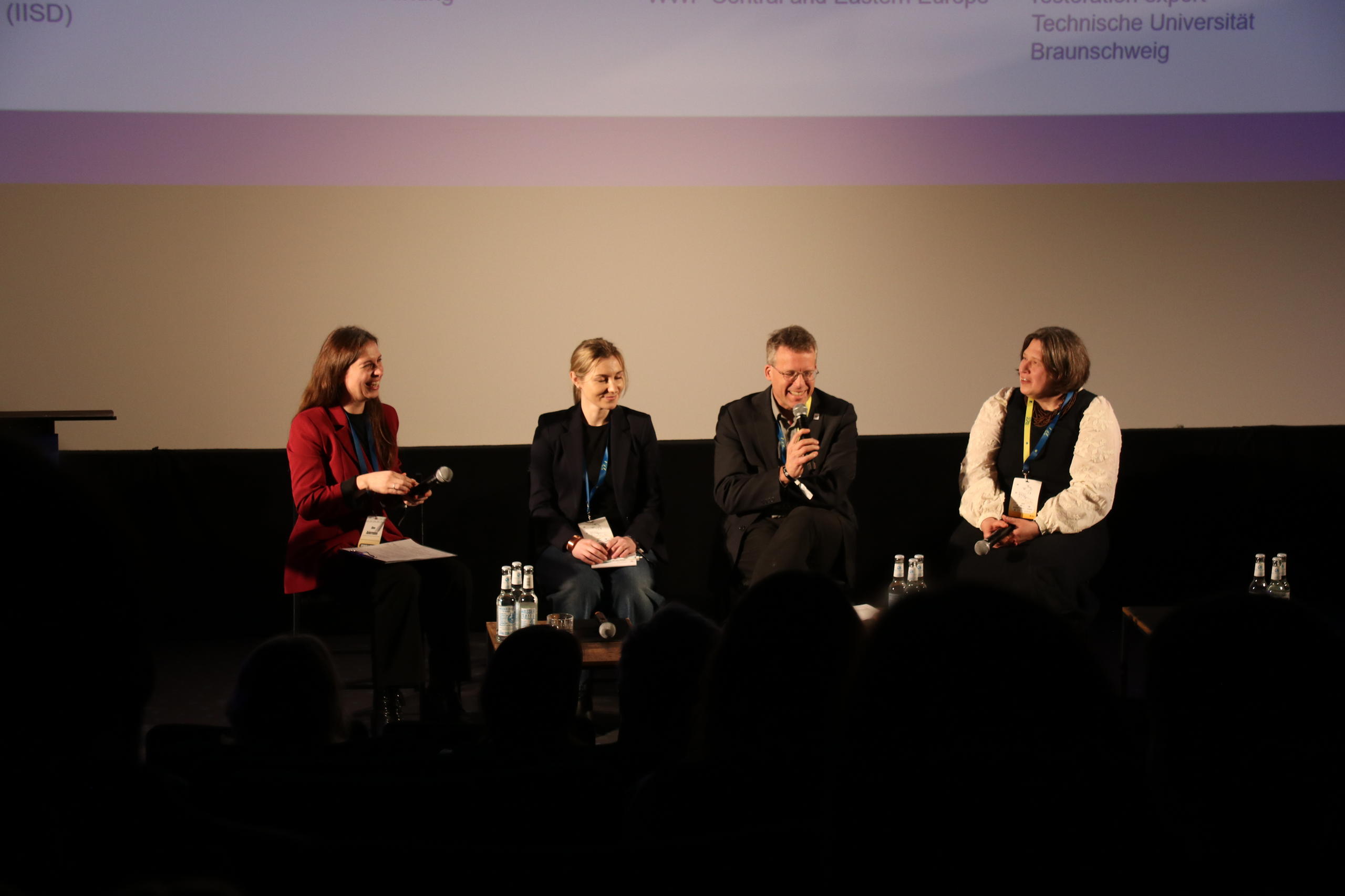 Foto von vier Menschen auf einem Panel, einer davon mit Mikrophon.